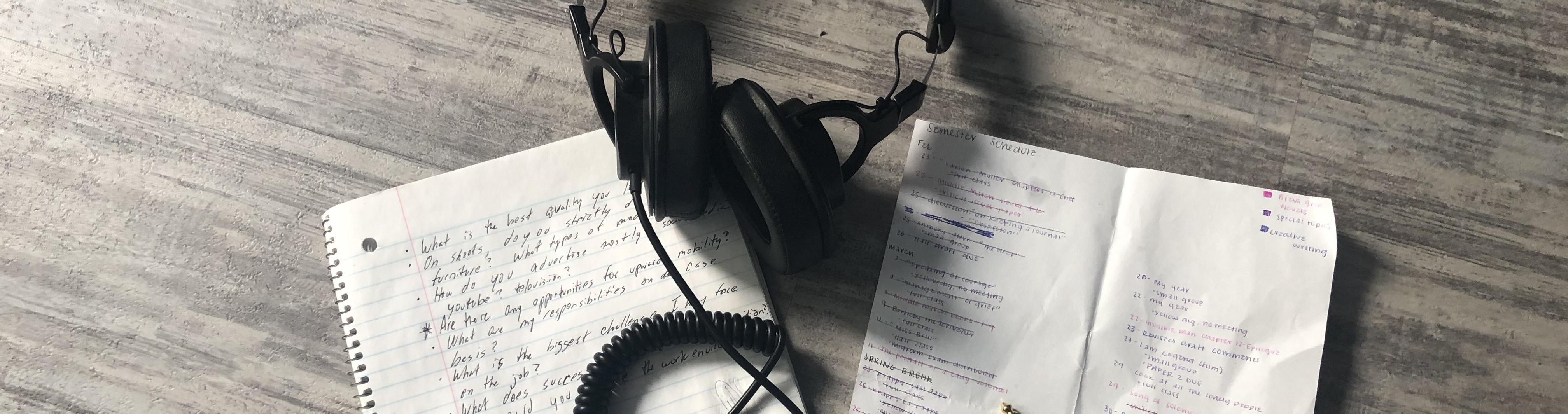 A pair of headphones and note paper on a gray wooden table.