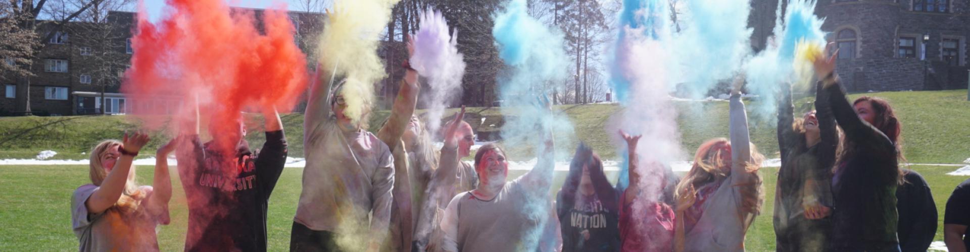 Students throw holi color powder into the air.
