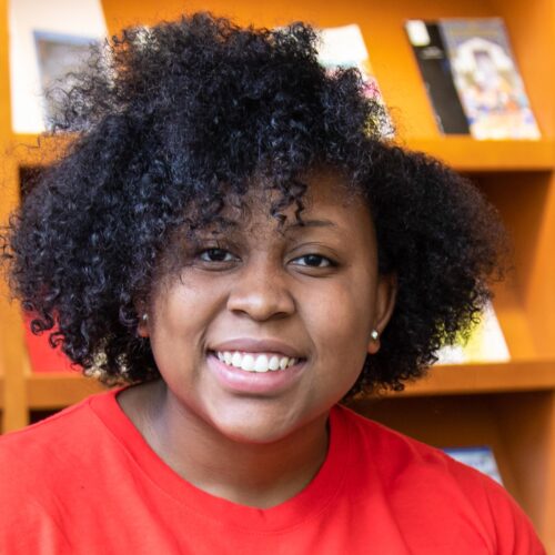 A woman sitting with a bookcase behind her