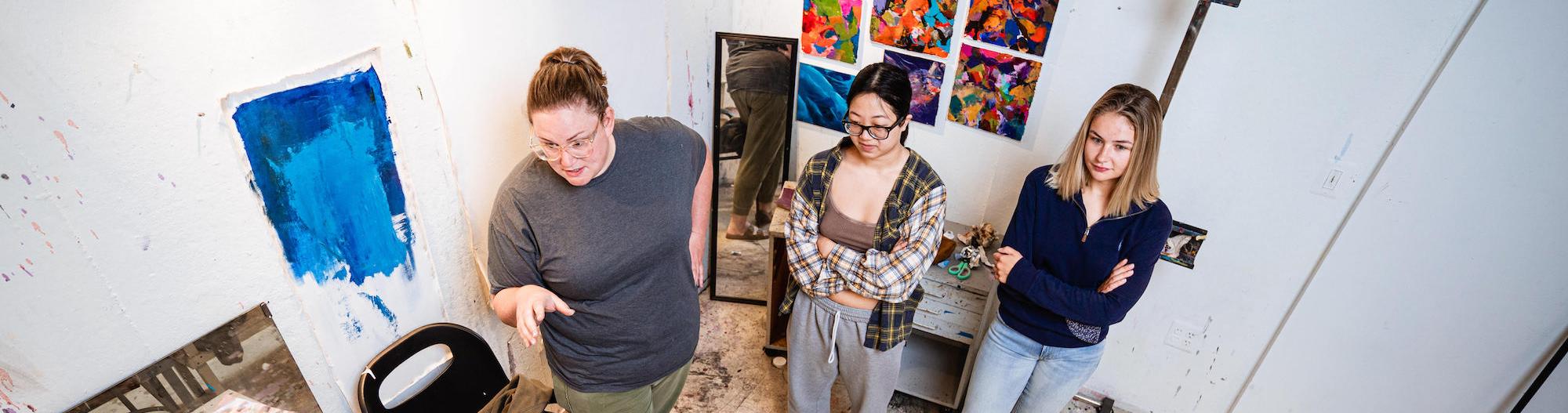 A photo of Krista Profitt and two other women by her side in front of a wall with blue paint on it