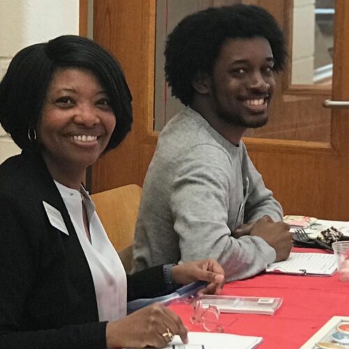 Two people smiling at the camera sitting down at a table