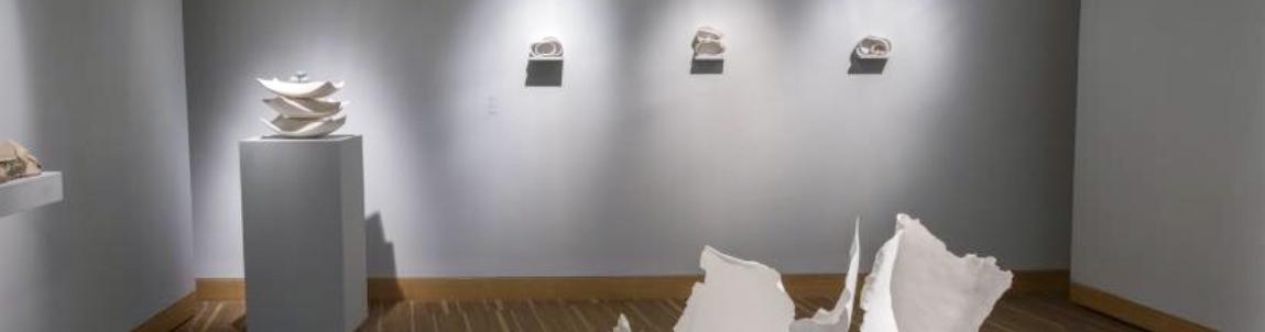 A mostly empty art gallery with the exception of a pillar containing three white dishes stacked on top of each other