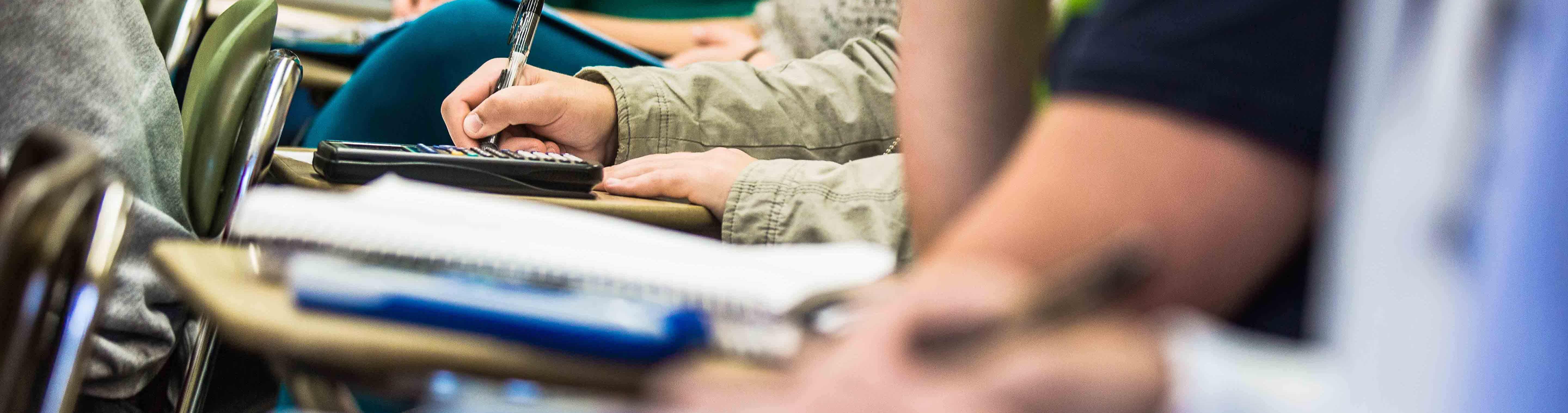 A photo of hands taking notes with a calculator on a desk