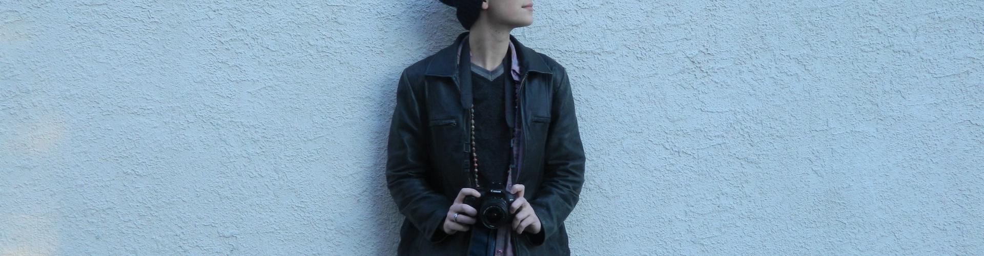 A person leaning against the wall carrying a Canon camera in their hands