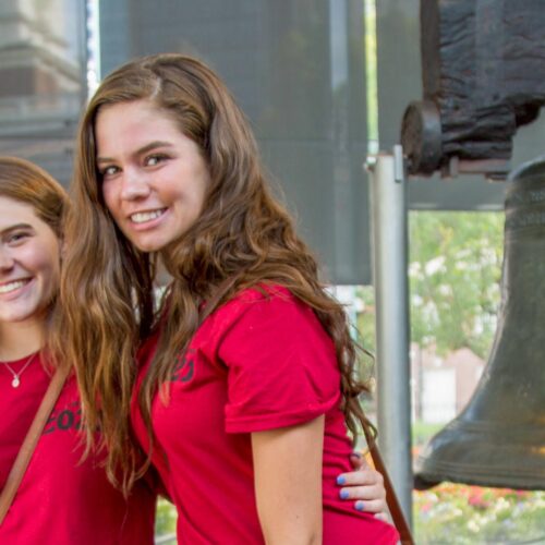 Three students wearing red shirts pose in front of the Liberty Bell