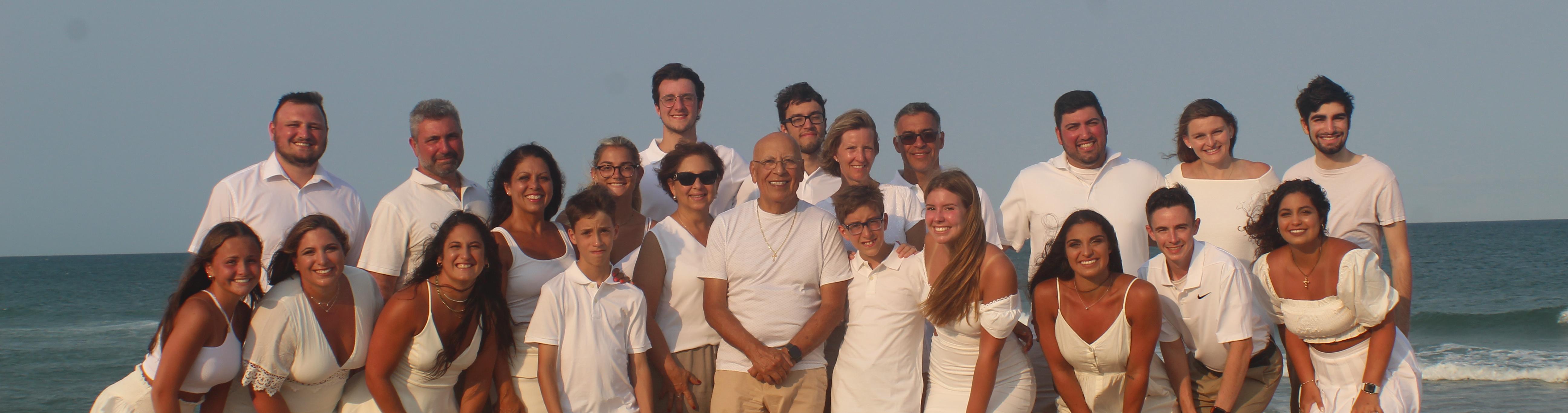 Group photo consisting of 24 people where white or off white on a beach.