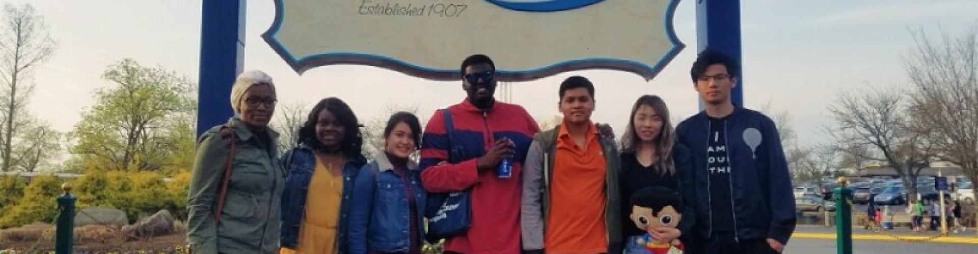 A group of people standing in front of a blue and white sign with one holding a stuffed doll