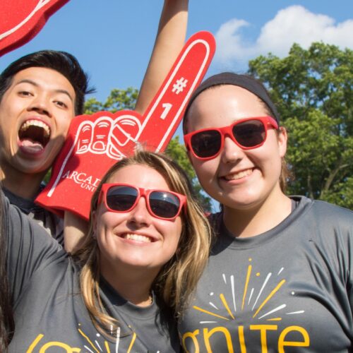 Four students wearing grey "Ignite" t-shorts and holding Arcadia foam fingers