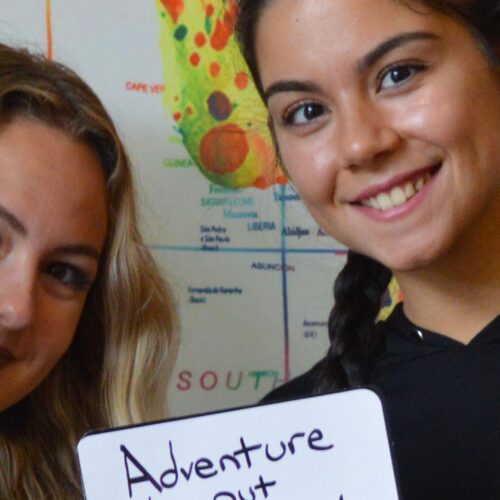 Two students stand in front of a world map