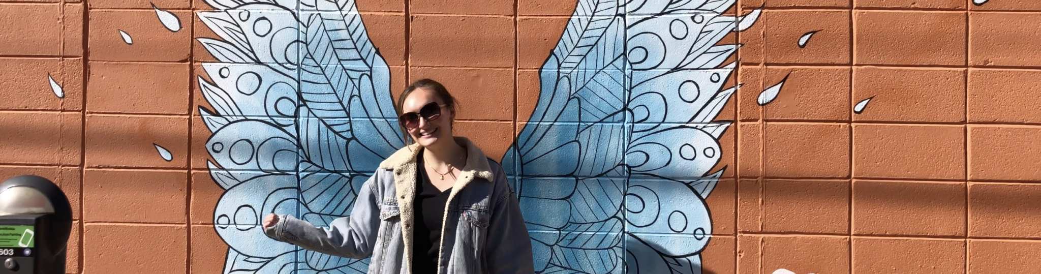 Student standing in front of painted wings.