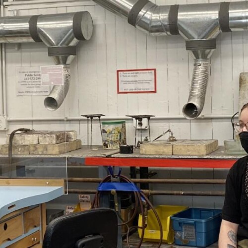 A masked teacher and student sit in the metal work lab.