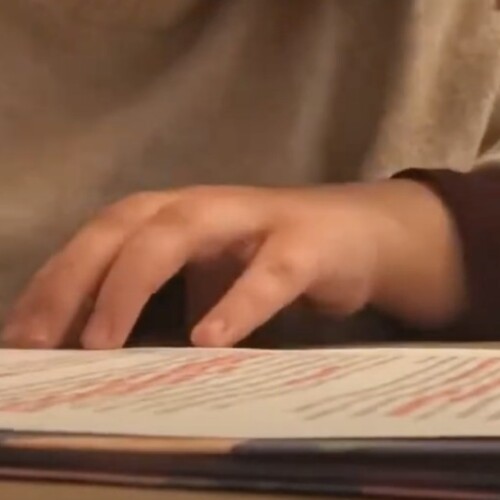 A student's hand holds a pink highlighter above a printed piece of paper.