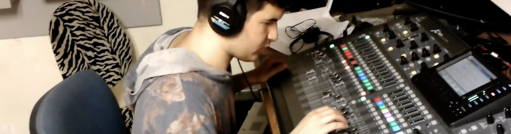 Male student working a sound board with headphones on and hand on sliders