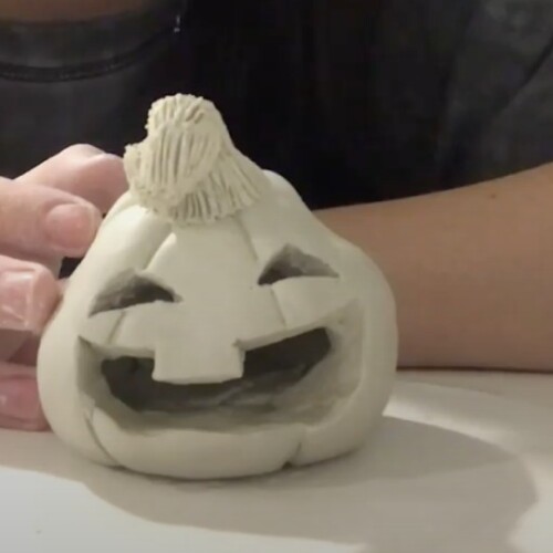 Someone making a ceramic jack-o-lantern pumpkin.
