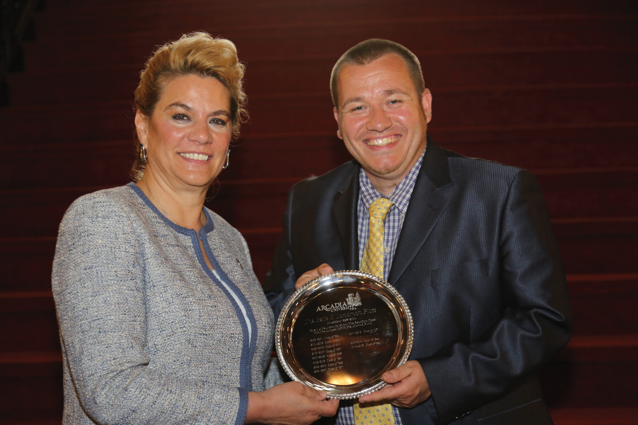 Two people on Grey Towers grand staircase holding an award plate