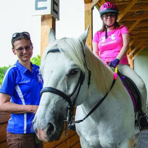 A person riding a white horse with the trainer beside