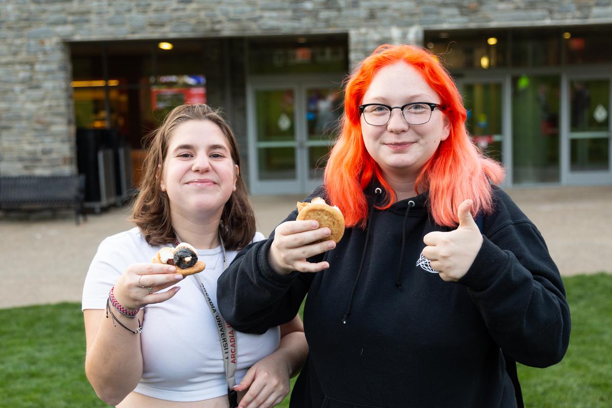 Two student smile and eat s'mores during homecoming & family weekend 