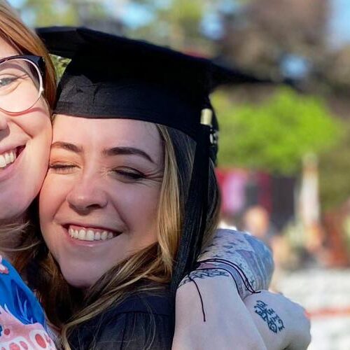 Student in cap and gown hugging friend