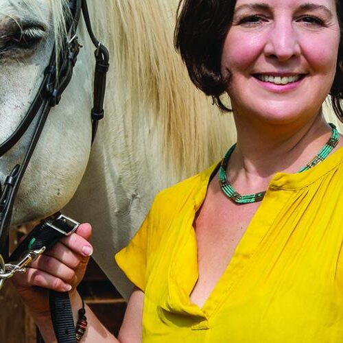 A woman holding a horse by her side