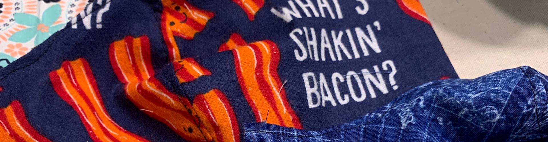 A navy piece of cloth contains strips of bacon and the words "What's Shakin' Bacon?"
