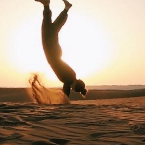 Two people doing hand-stands on a beach.