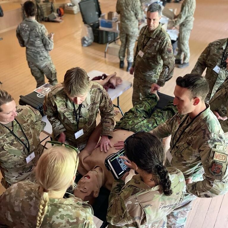 A group of military medics standing over a training dummy to learn medical techniques.