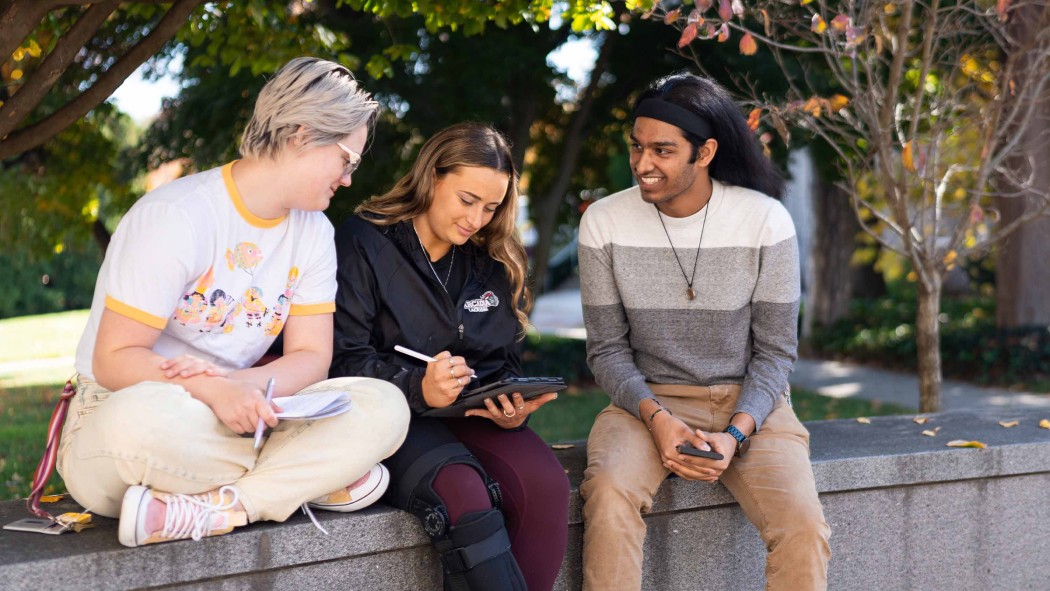 Arcadia students sitting on a wall on campus in the Fall.