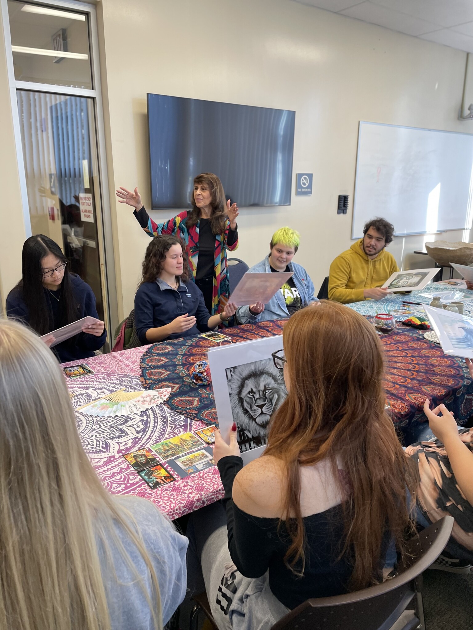 Linda Ruth Paskell waves her hands at a table of six students each holding artwork in their hands