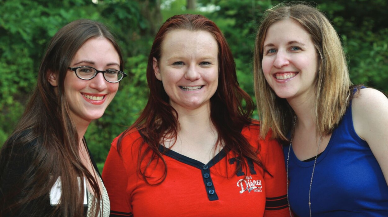 Three young female alumni smile at camera