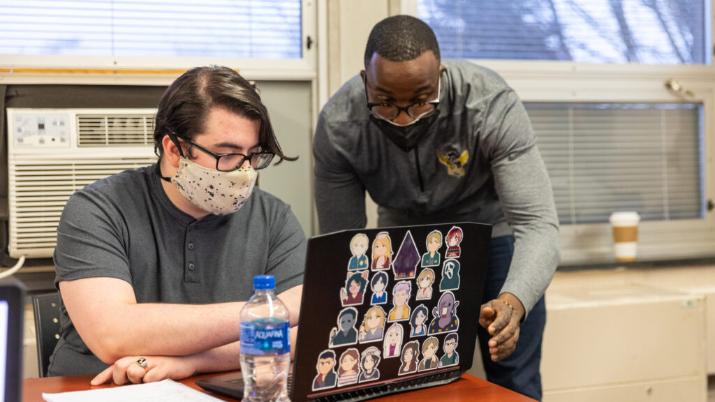 Professor works with a student on a laptop.