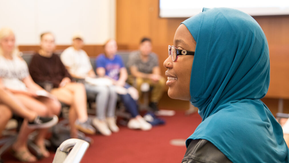 Profile of a student smiling during class. Other students are seated in the background.