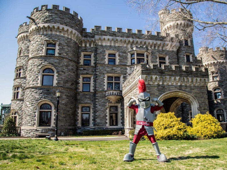 Archie the Knight mascot flexes in front of Grey Towers Castle.