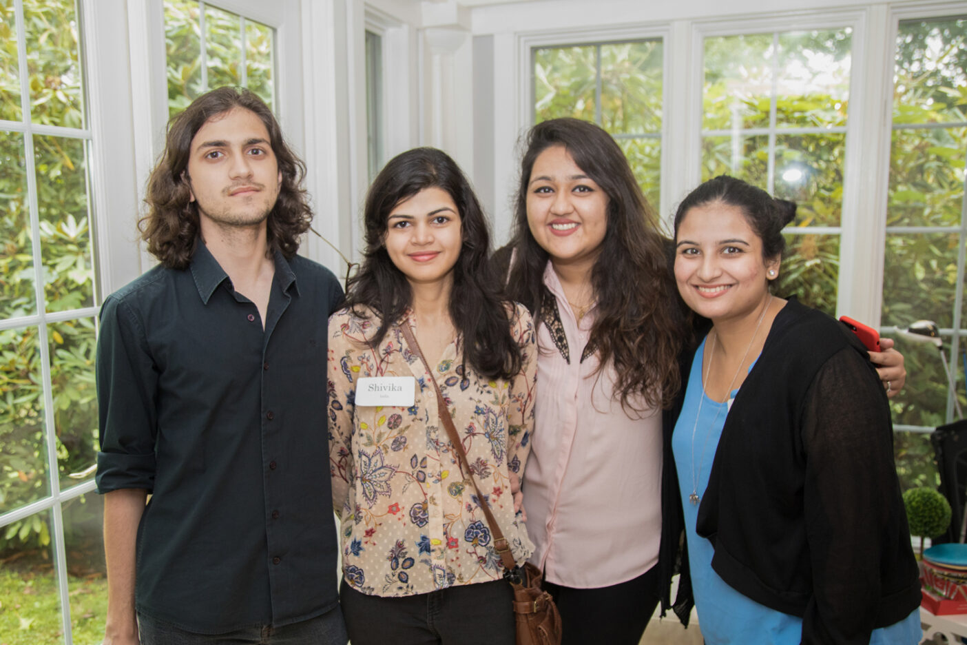 Four international students smiling at the camera while standing in a garden room.