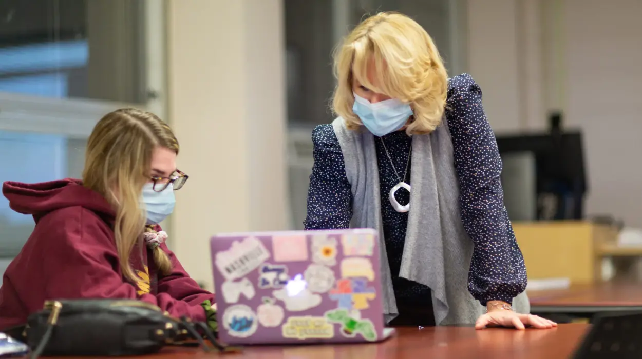 Professor works with a student on a laptop.