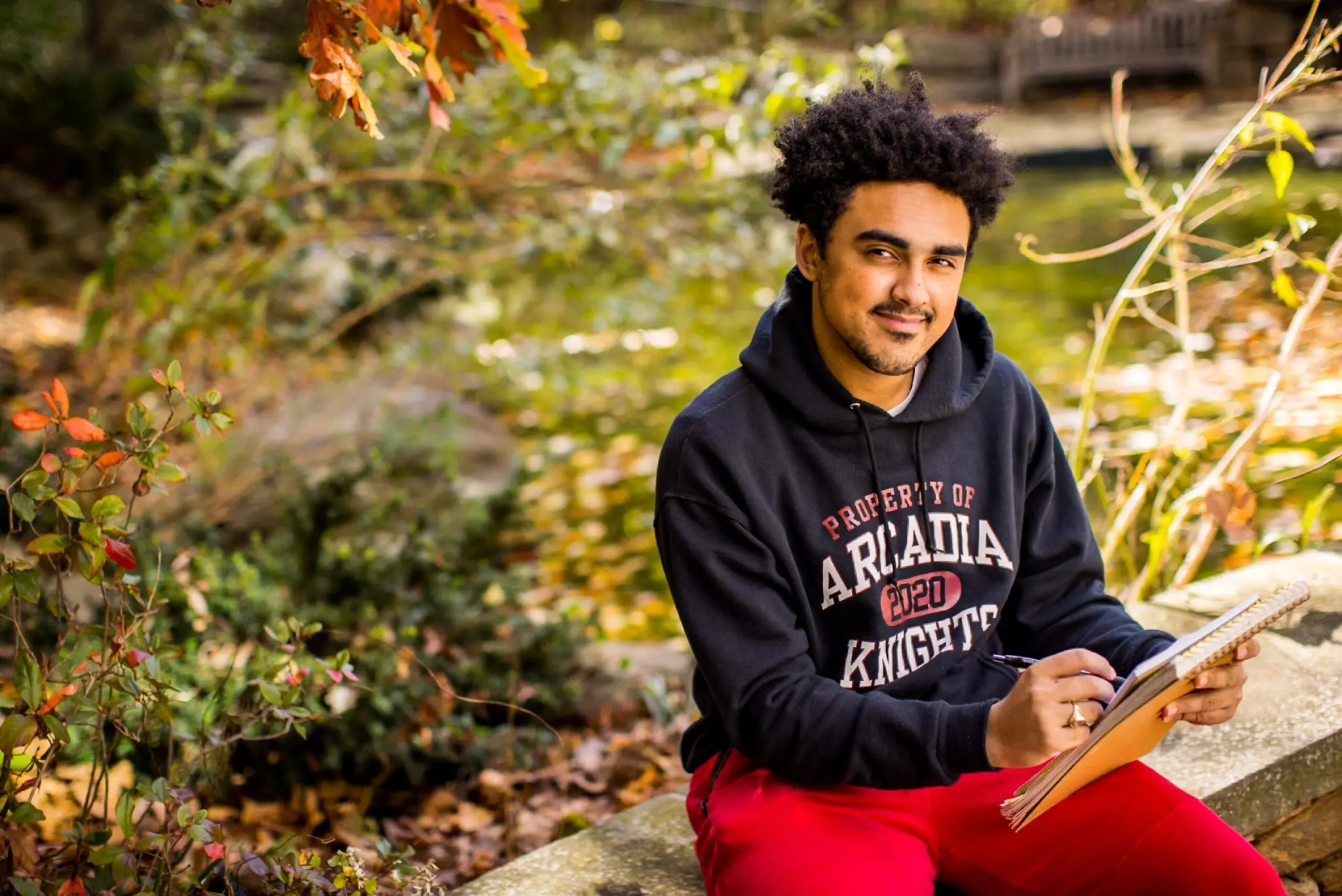 Gavin Meyers sits near a pond and writes on a notebook