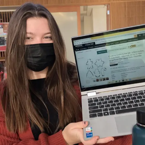 Student in face mask holding up laptop with internet browser open