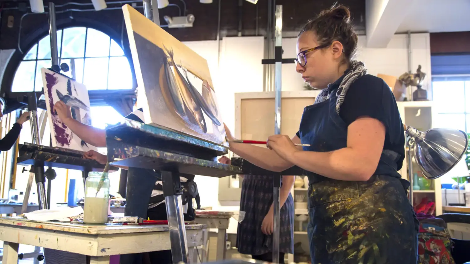 Students work upright on canvas paintings in an art studio
