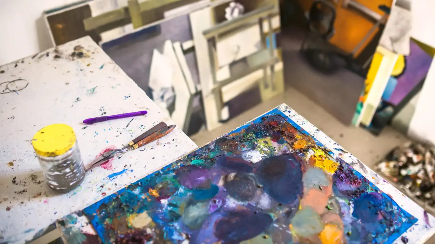 A canvas with blue and yellow paints and pallet knife rest on a table in an art studio