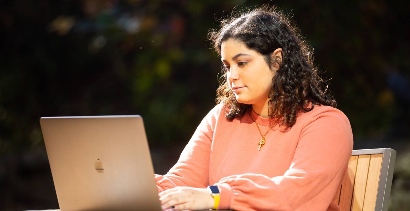 Student sitting outside at a table while using laptop.