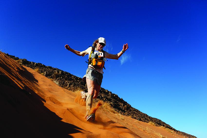 An woman runs down a sand dune.