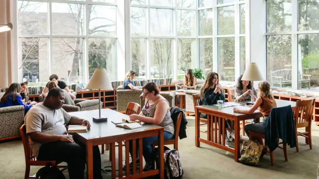 Students sitting at tables while working in library.