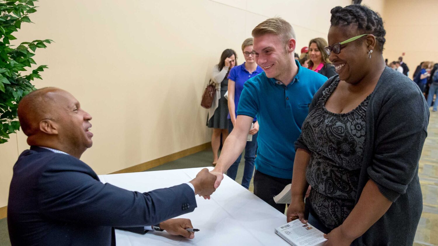 Two students smile and shake the hand of author, Bryan Stevenson.