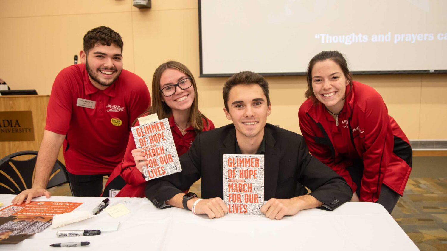 Three Arcadia students pose smiling with activist, David Hogg, and his book