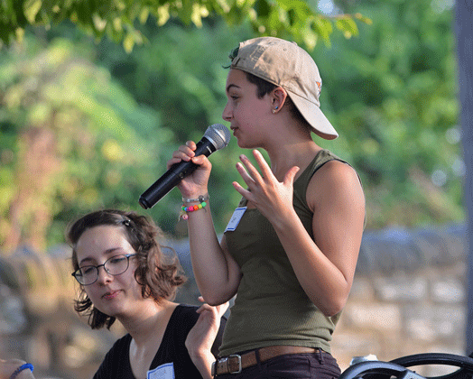 Deb, a speaker for the Honors Program, talking into a microphone while outside.