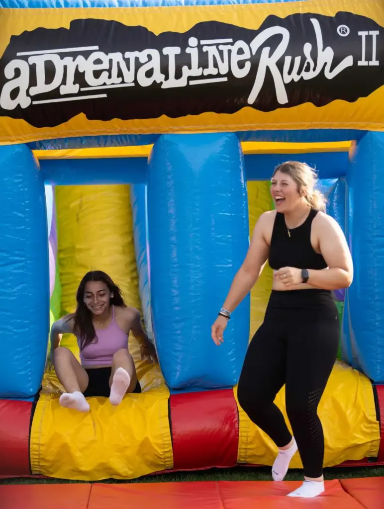Two students sliding down bounce house during Blitz Spring Fling