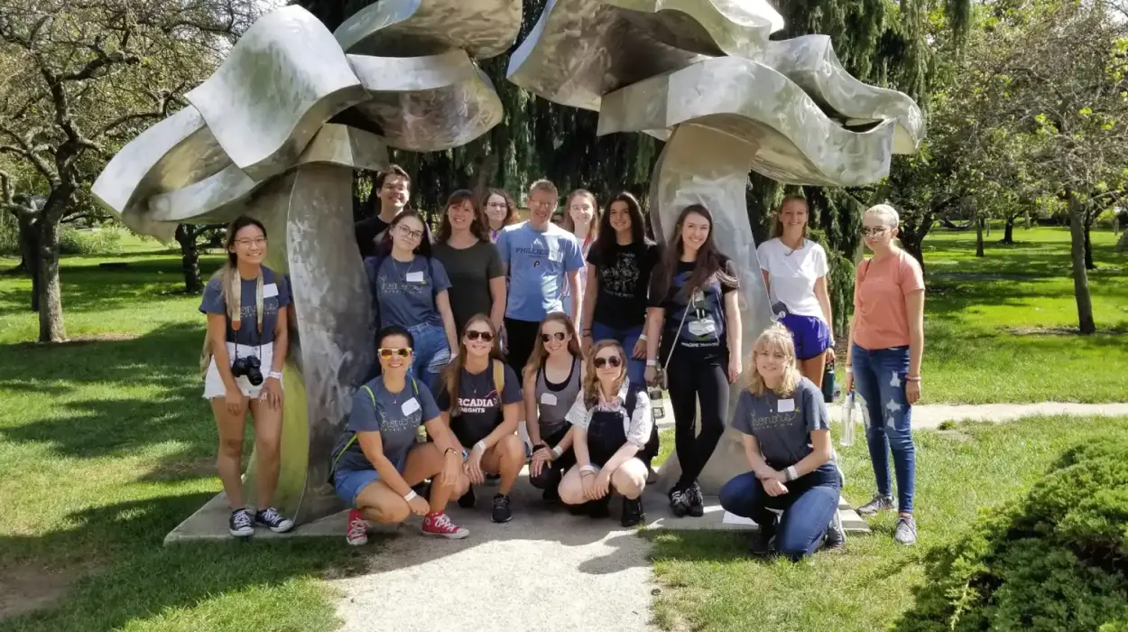 Honors students stand around an outdoor art sculpture.