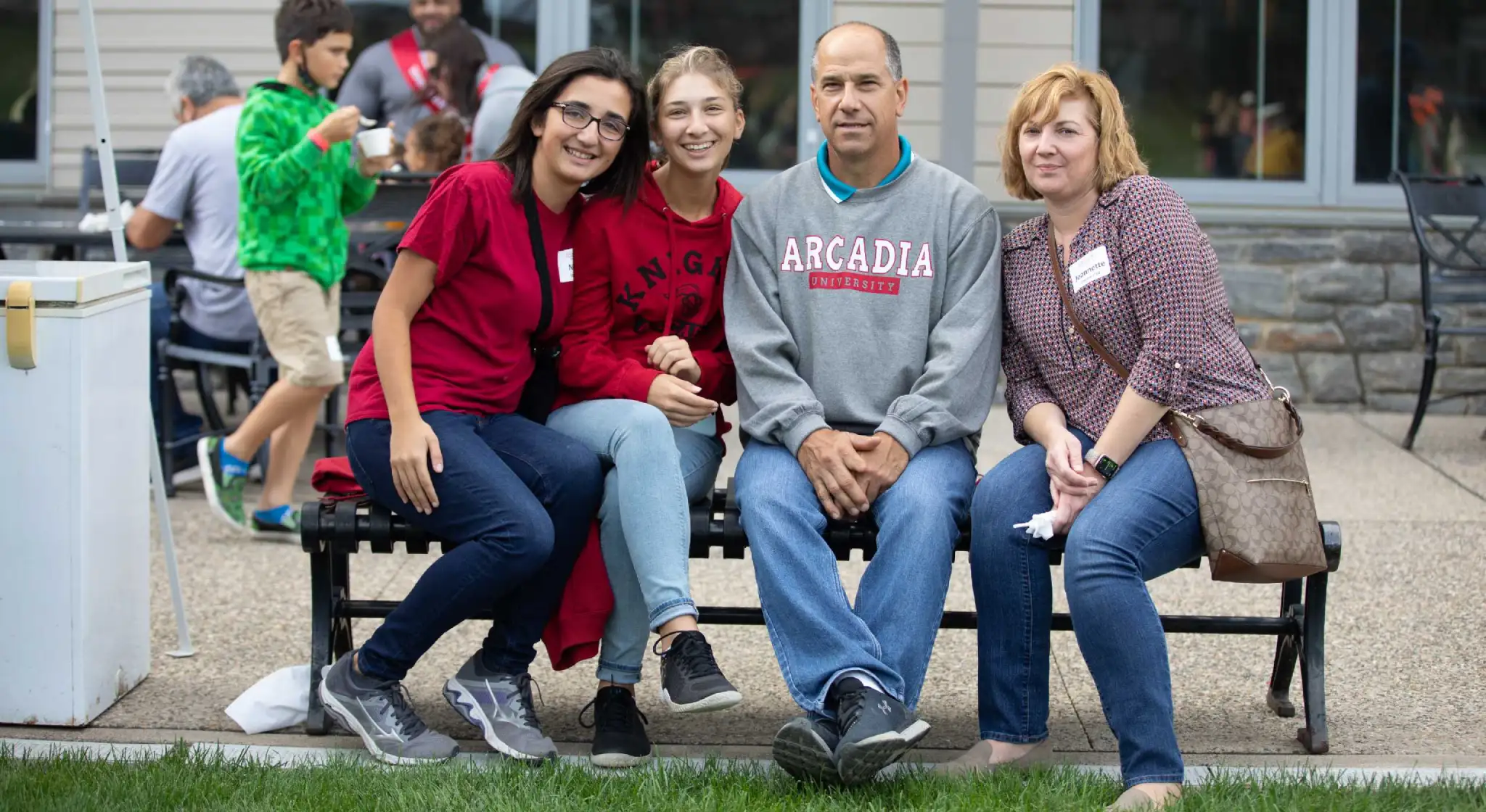 A family of four sitting on a bench outside while smiling at the camera during homecoming weekend.