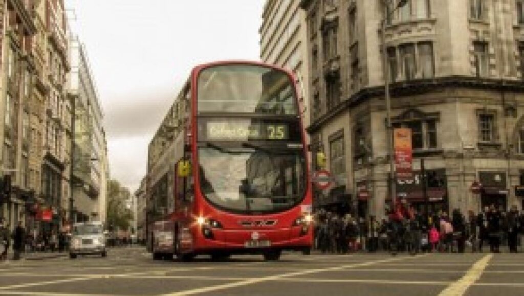 A red double-decker bus on a Victorian street in London, England.