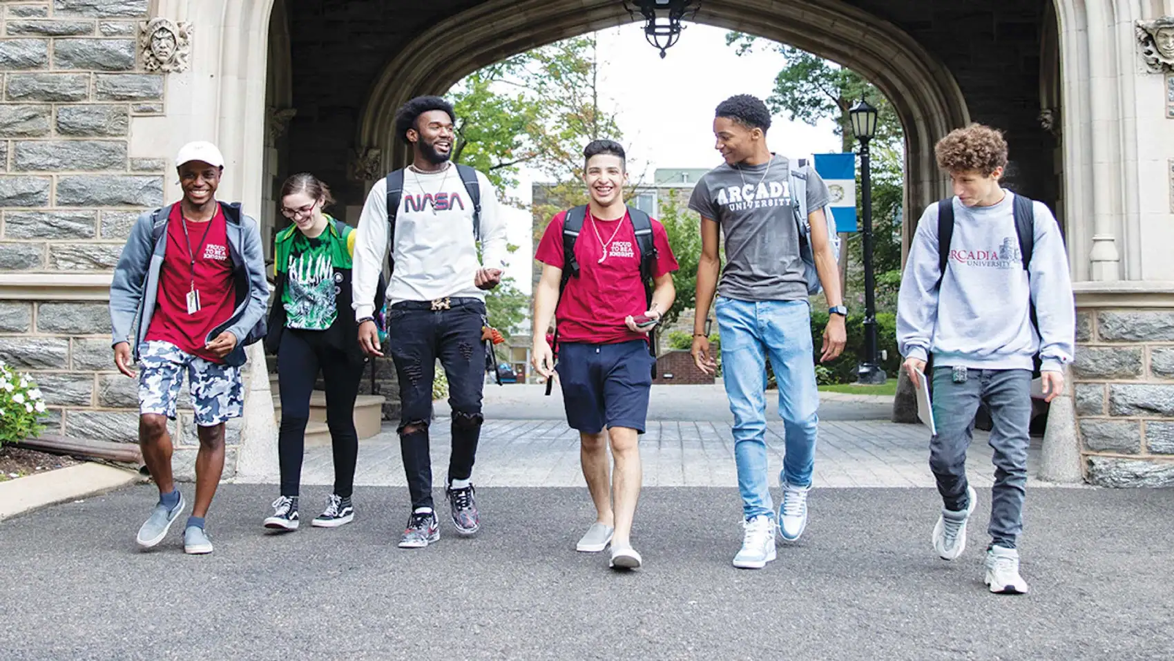 Six students walk through an old stone archway at Arcadia University.