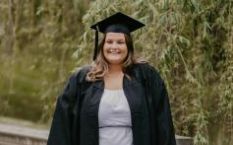 Catherine Bergmueller posing on a bridge and dressed in graduation attire
